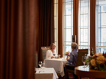 A couple dining at a table covered with a white tablecloth, next to a window at RACV City Club's Members Lounge.