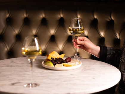 A hand holding a glassof wine near a small plate of food. 