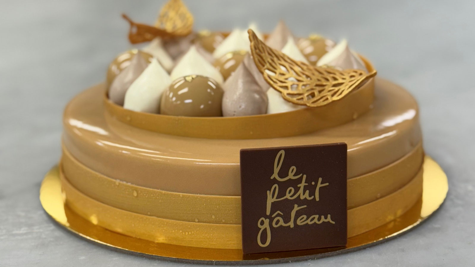 A brown glazed cake with dollops of cream and gold leafing. 