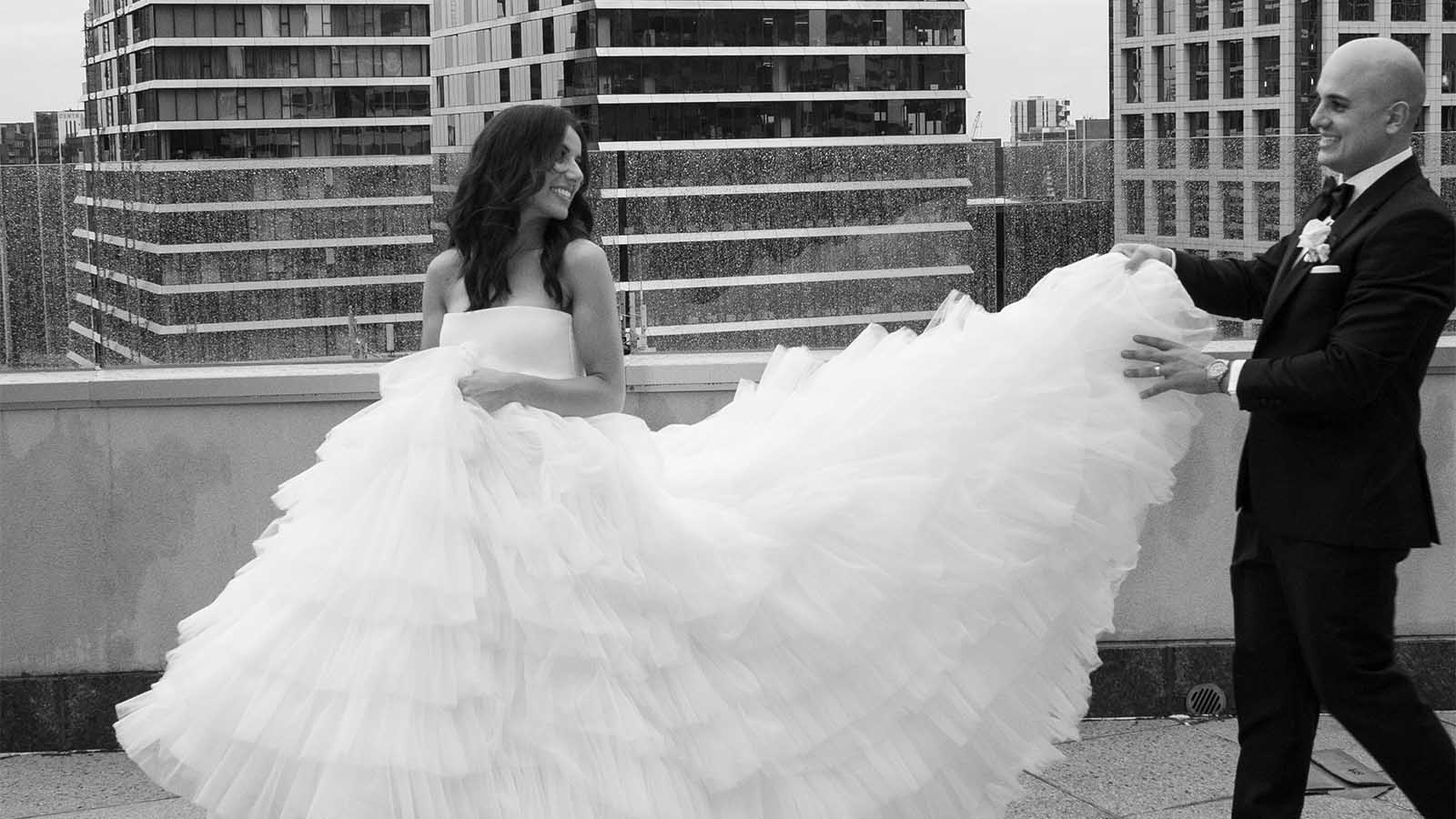 Groom holding the Brides dress, while posing for a photo on the City Club's balcony.