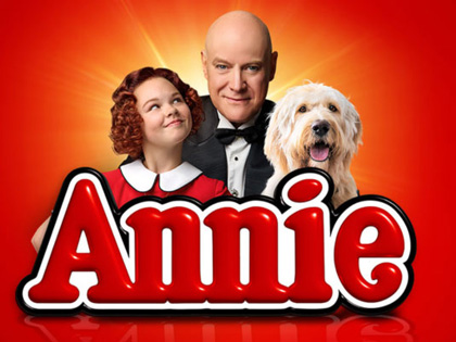 A poster of Annie the character looking up at a man in a suit with a dog next to them. 