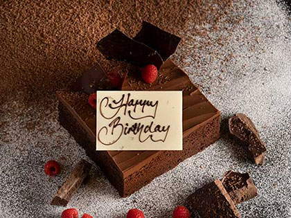 A piece of chocolate cake with happy birthday plaque.