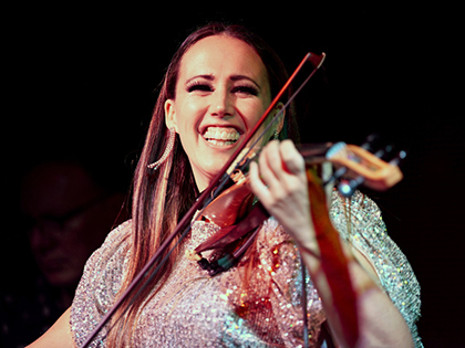 Female violinist playing a violin and smiling at the camera.