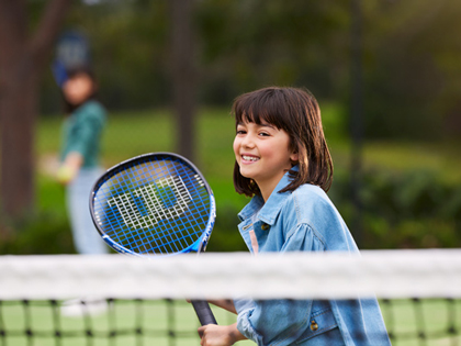 A child smiling and playing tennis on the courts at Healesville Country Club and Resort.