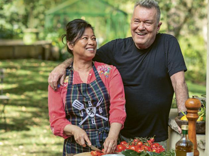A couple cooking together outside.