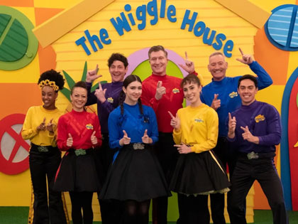 The wiggles posing infront of a colourful back drop. 