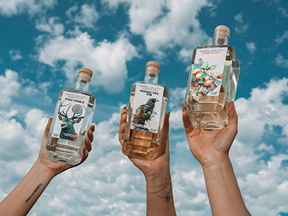Three hands holding three bottles of vodka aloft in the sky.