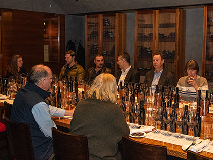 Group of people sitting around a table filled with wine glasses and wine bottles.