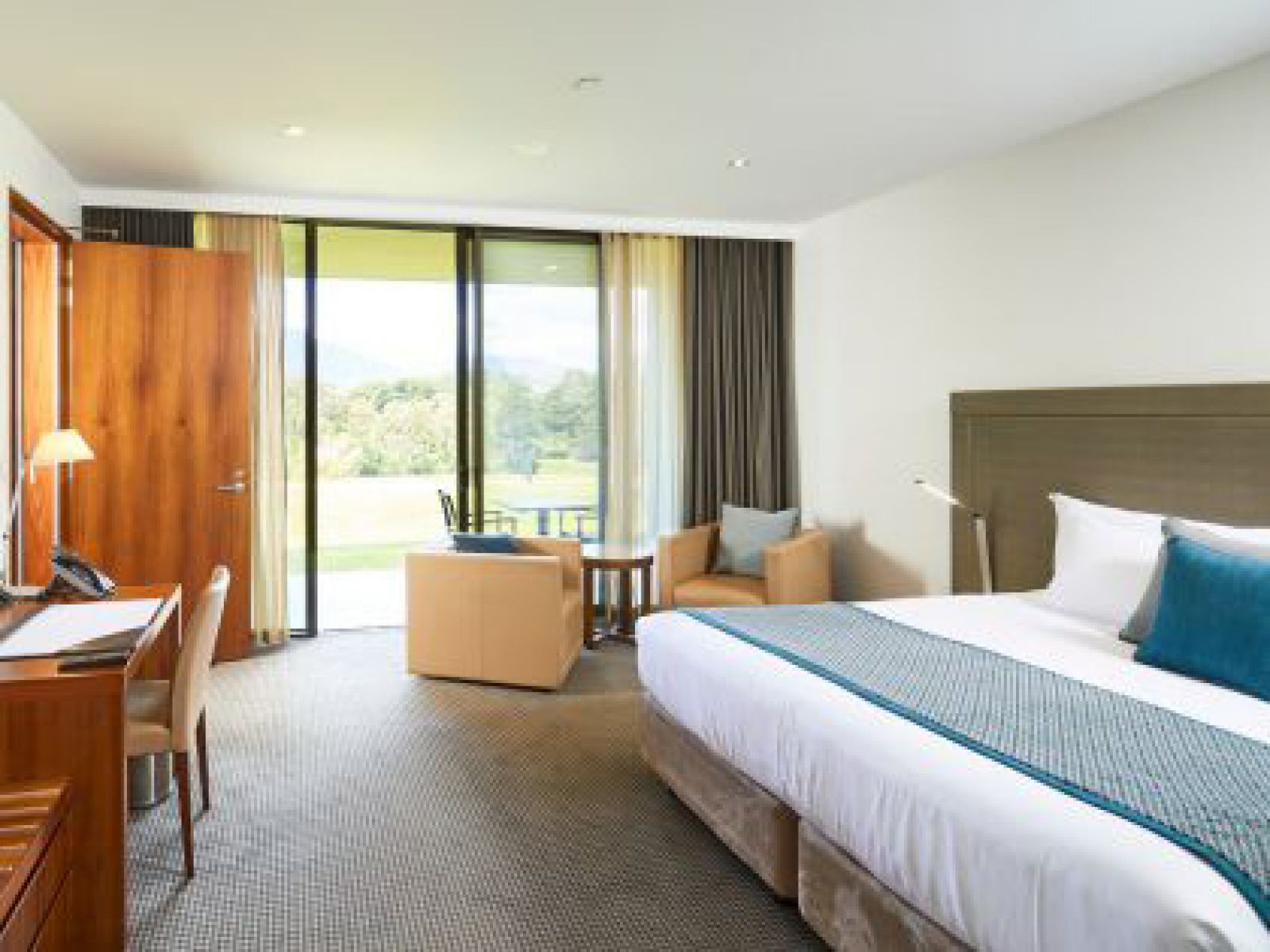 Mountain View Family Room with the sliding doors open showing green grass, featuring a king sized bed, desk and chairs.. 