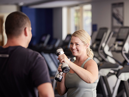 Person working out with dumbbells at RACV Healesville Country Club & Resort's fitness centre, while a trainer supervises.