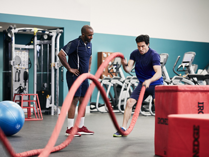 Man swinging large red ropes with his personal trainer encouraging him in the helaesville fitness centre. 