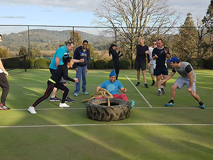 Team dragging team member on a large tyre outside as part of a team building activity.