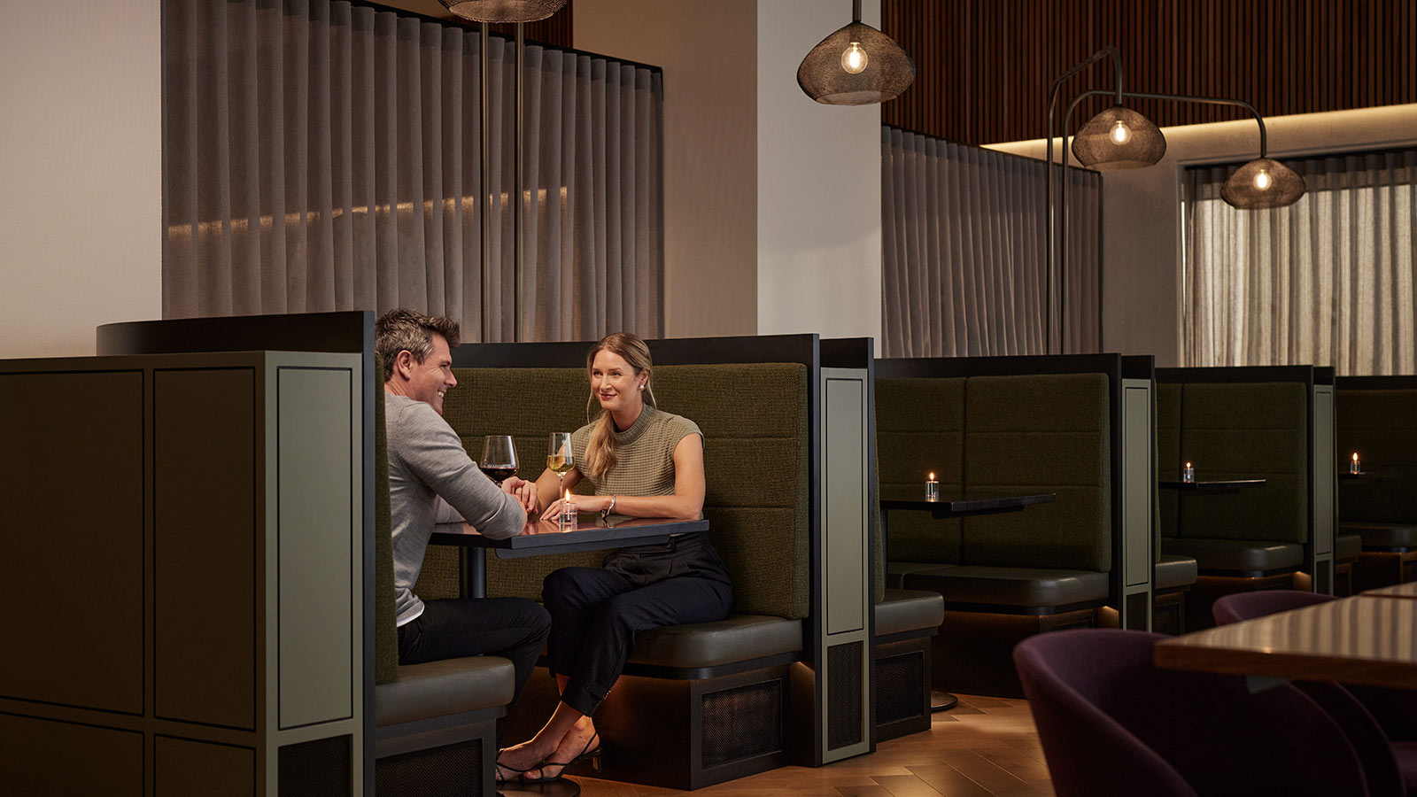 Two people sitting in a booth and drinking wine opposite each other at Banyalla, RACV Healesville Country Club and Resort.