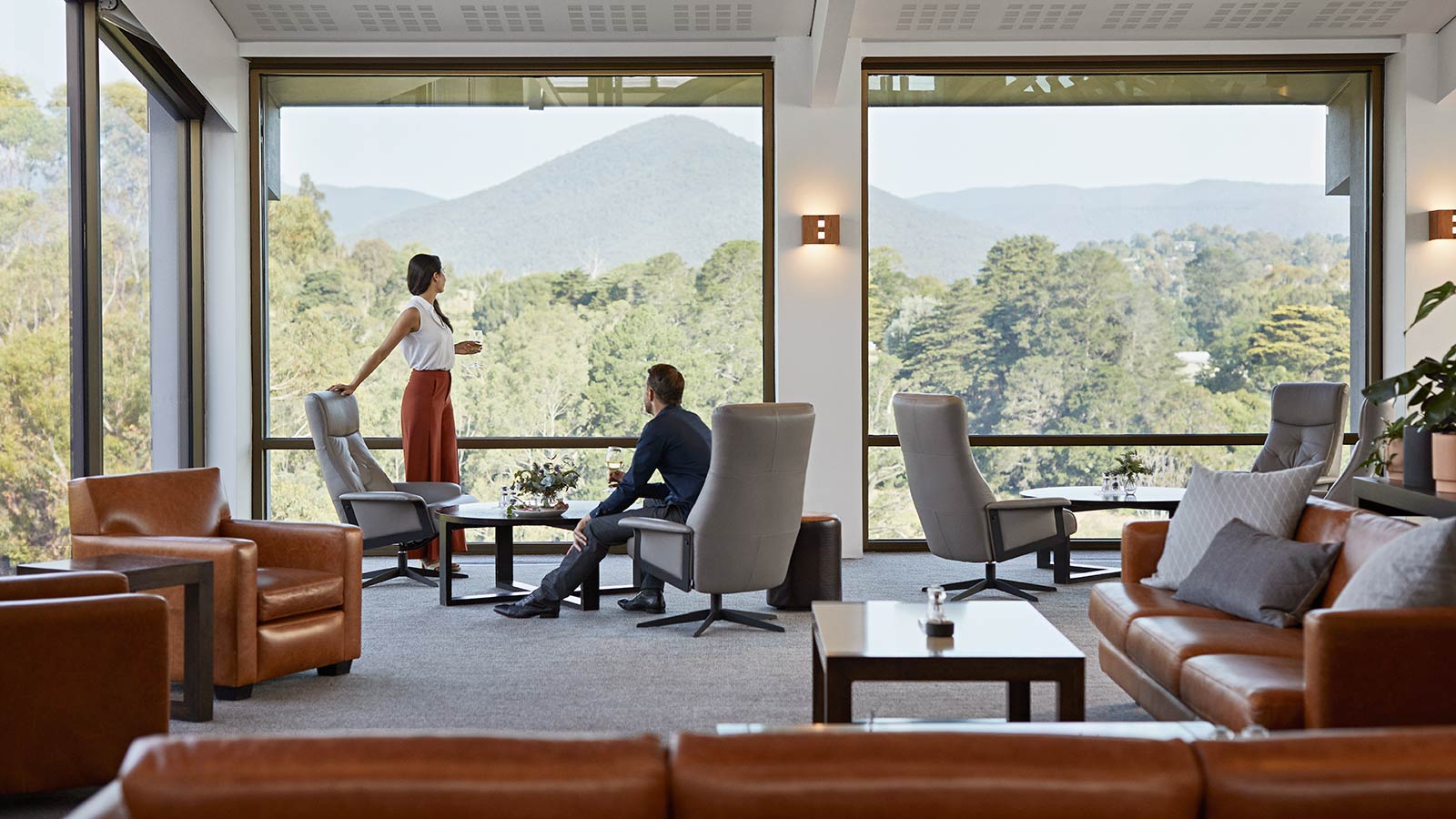Two people drinking wine and looking out at mountain views from the Members' Lounge at RACV Healesville Country Club and Resort.