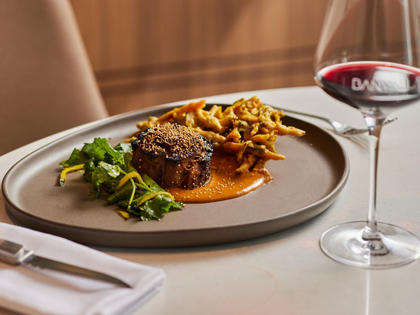 Meat and greens on plated dish with red wine glass on the side at Banyalla restaurant at RACV Healesville Country Club and Resort.