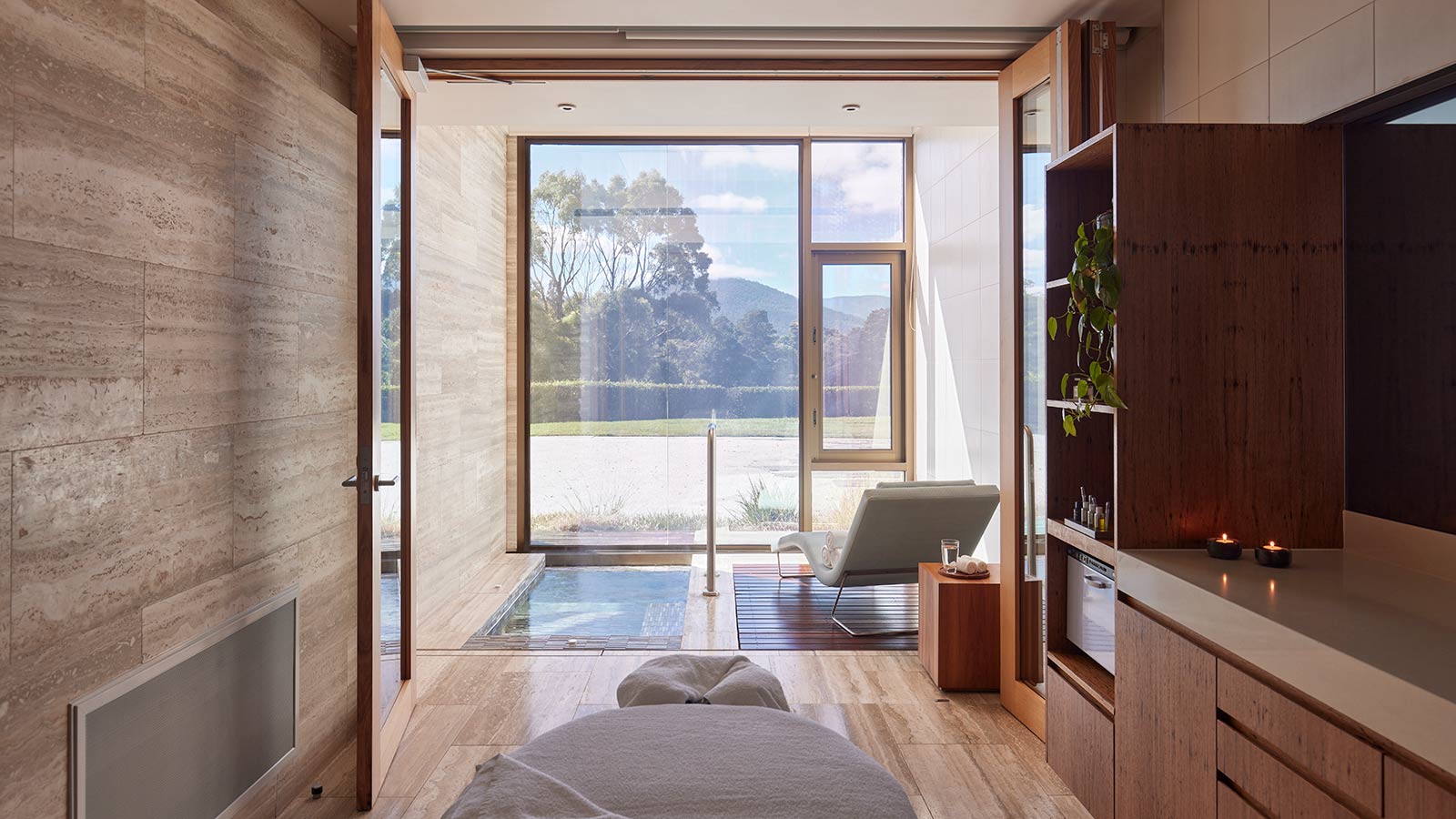 Treatment room at RACV Healesville Country Club and Resort's One Spa, featuring a treatment bed, shallow pool and lounge chair facing a floor-to-ceiling window.
