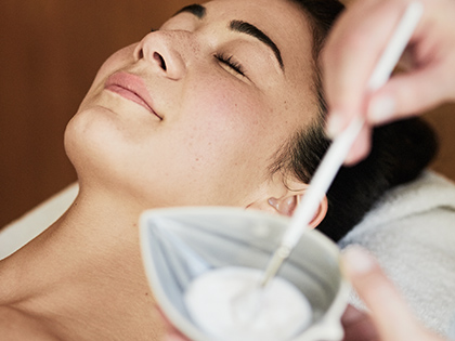 Person lying down in a treatment room at RACV Healesville Country Club & Resort's One Spa, while a beauty therapist prepares their facial.