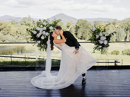 A bride and groom kissing on the deck in front of the gardens and mountains at RACV Healesville Country Club.