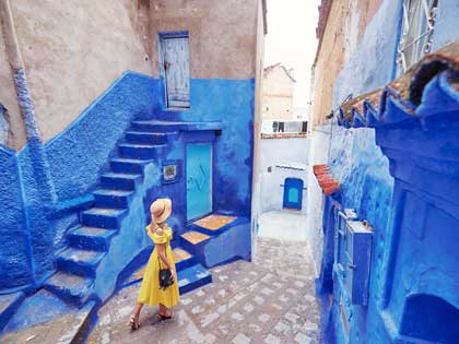 Young woman in yellow dress walking in the streets between painted blue houses.