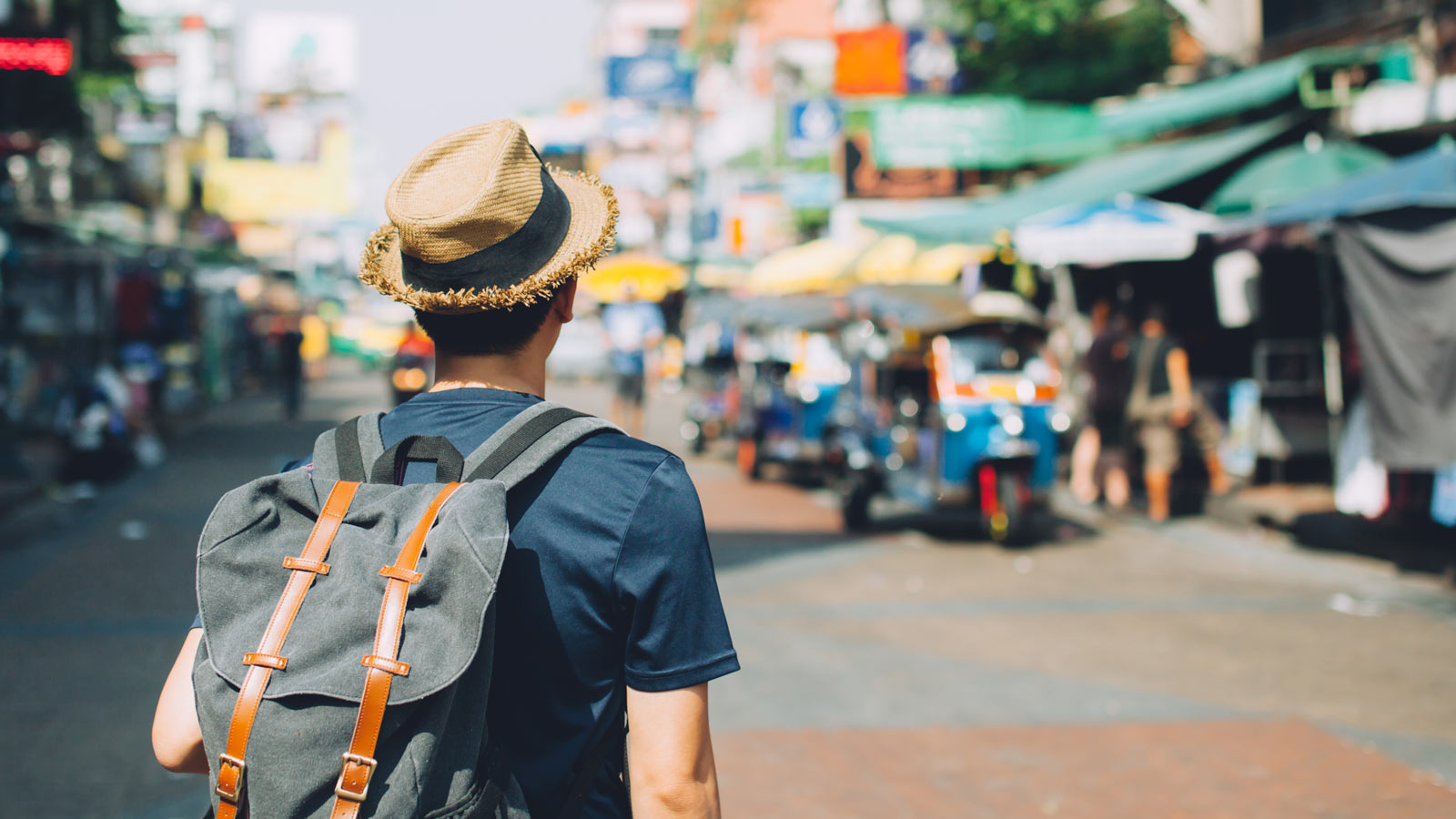 A backpacker wearing a hat in a sunny city.