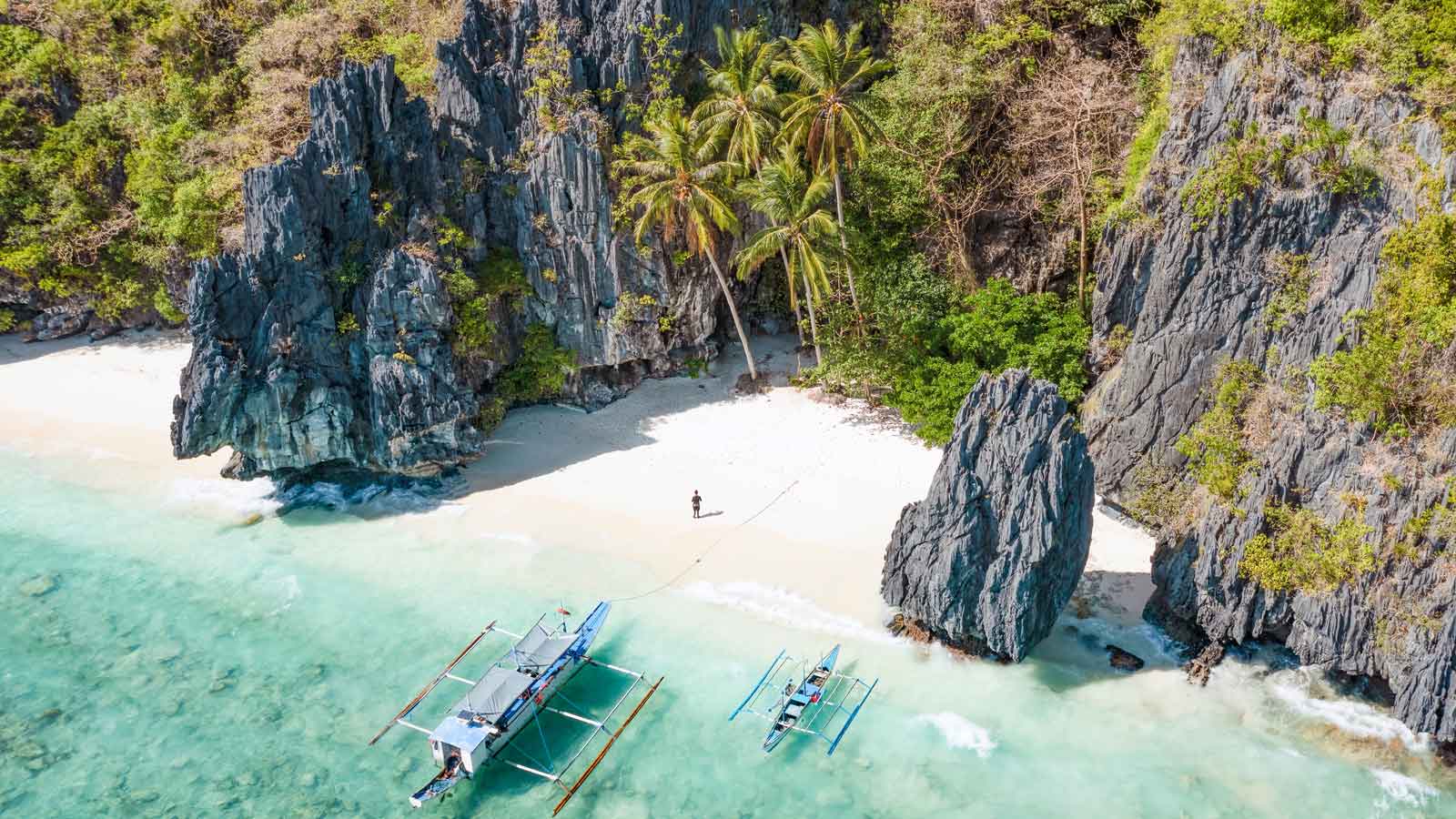 Aerial view of crystal clear waters on a shoreline in the Phillipines with white sand , cliffs and palms.