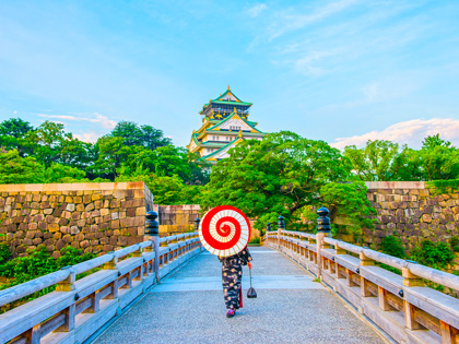 A walking Geisha holding an umbrella heading towards a temple