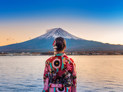 Woman in traditional Japanese clothing looking across the water at Mount Fuji