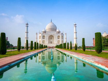 A beautiful while building in India with its reflection shinign in the water lined with trees. 