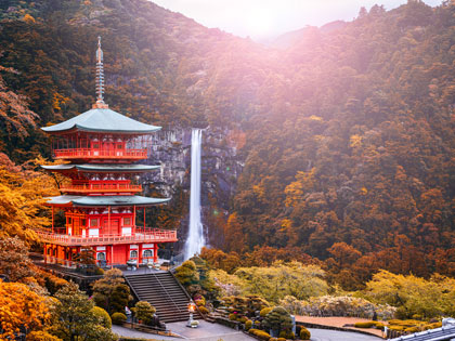 A large red temple next to a cascading waterfall