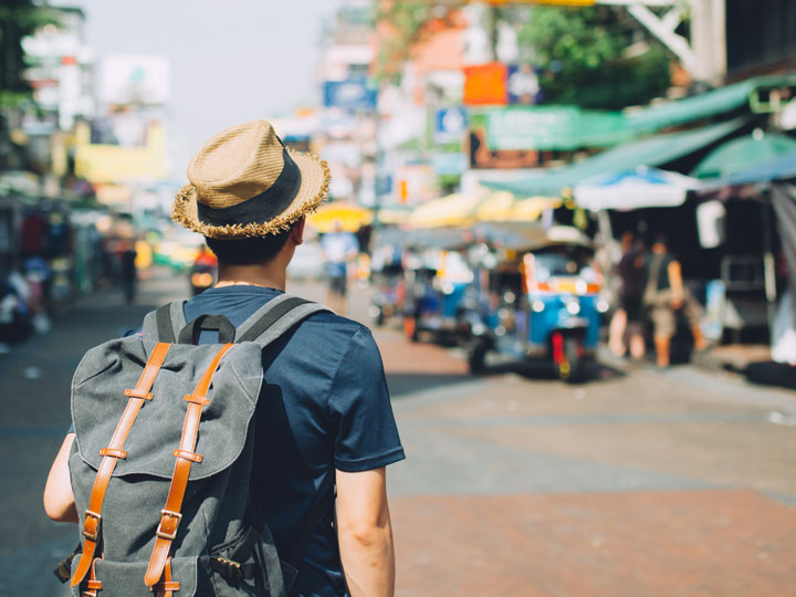 A backpacker wearing a hat in a sunny city.