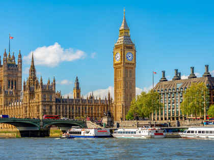 Big Ben with a blue sky in the background and boats on the river