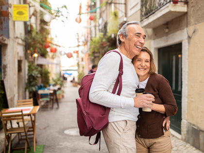 Senior tourist couple hugging posing with backpack outdoors
