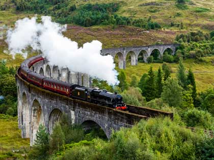 Steam train in Scotland coasting along a bridge in a lush green landscape