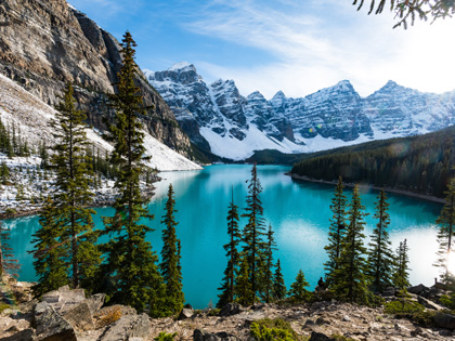 Glacier blue lakes surrounded by rocky snow covered mountains and pine trees.
