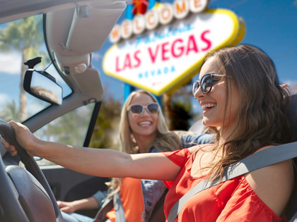 Two girls in a convertible car driving by a Las Vegas sign.