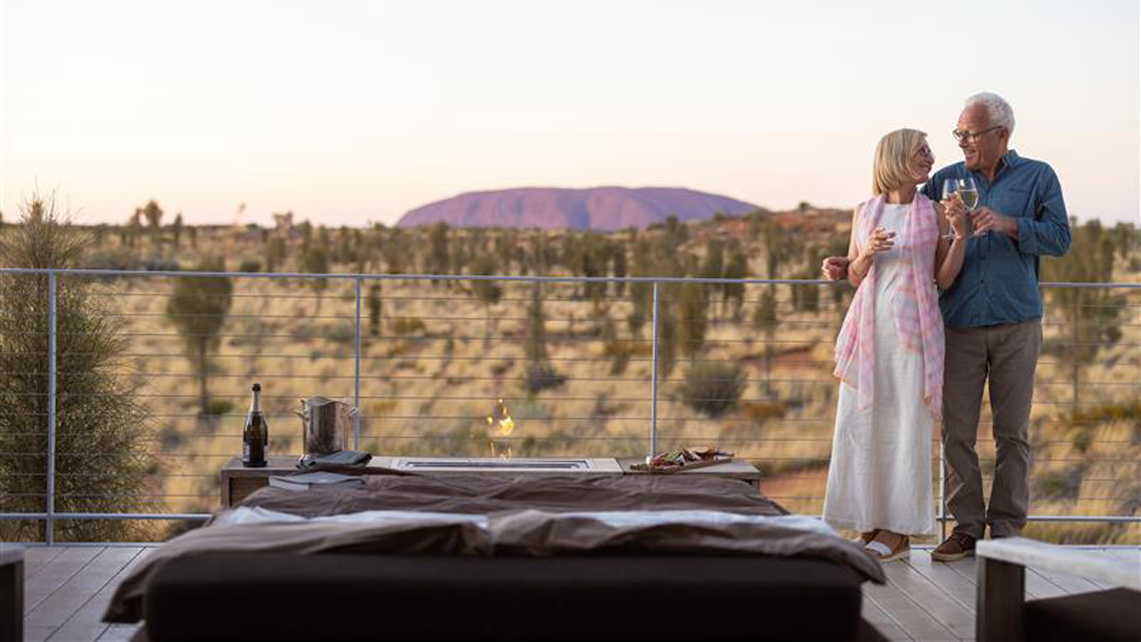 A couple dining on a balcony overlooking Uluru.