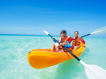 Two kids kayaking in an orang kayak in crystal clear waters.