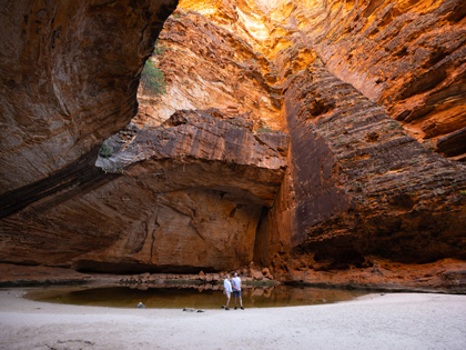 People standing below some big rock cave with waterpooling down the bottom.