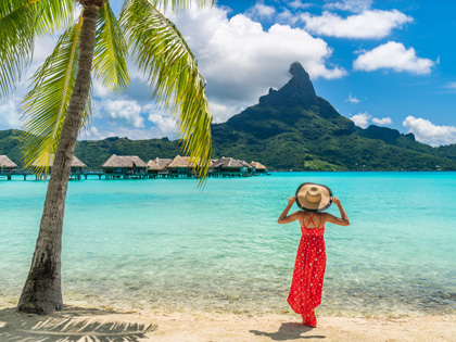 Woman walking on Bora Bora island enjoying holiday in Tahiti, French Polynesia with Mount Otemanu and overwater bungalows villas hotel landscape.