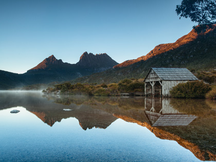 Early morning light illuminates mountain peaks reflecting in the calm waters  of a lake. 