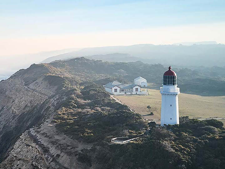 White lighthouse overlooking cliffs and rough waters.