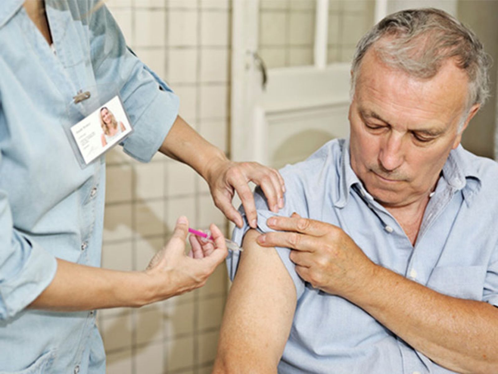 A man with his sleeve rolled up getting a travel vaccination from a nurse. 