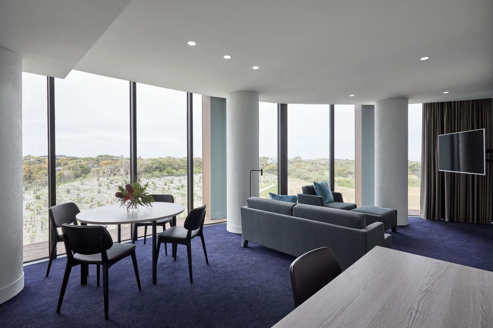 The living area of the Spa Family Suite at RACV Cape Schanck Resort, with couches, a modern kitchen, and floor-to-ceiling windows with views of the scenery outside