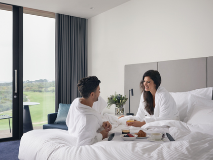 Couple enjoying breakfast on the bed in the peninsula suite. 
