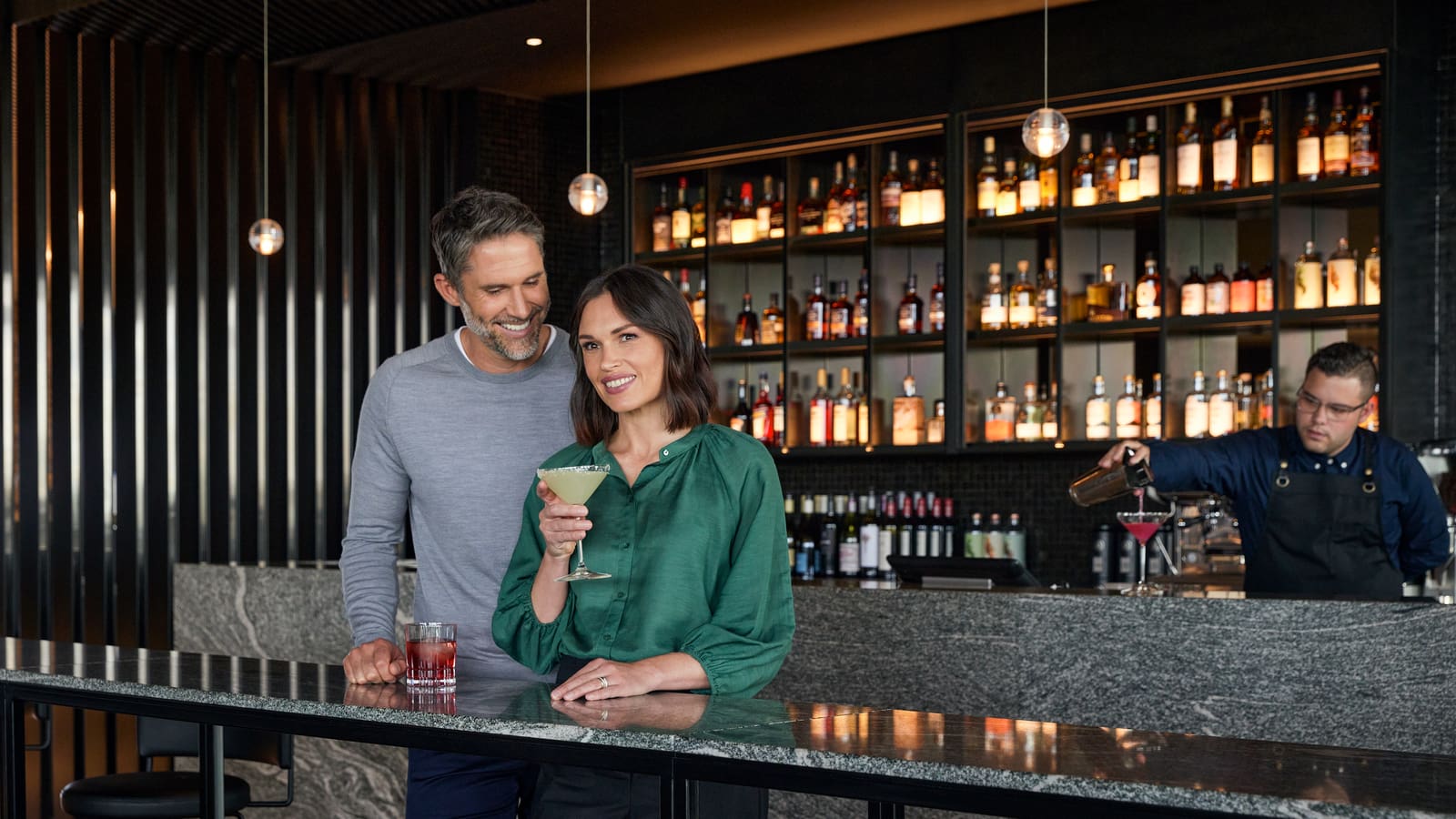 Couple standing in RACV's Cape Bar, smiling and drinking cocktails.