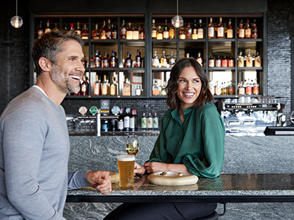 Couple sitting at RACV's Cape Bar, laughing with drinks and a dessert plate on the table in front of them.