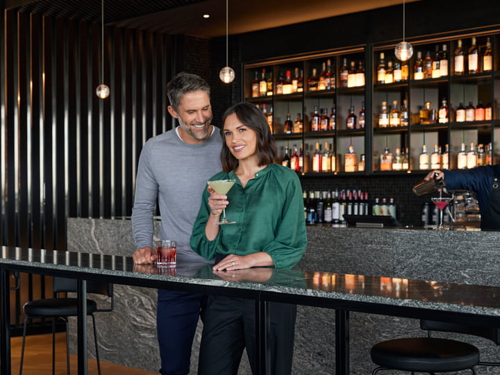 Couple standing in RACV's Cape Bar, drinking cocktails.