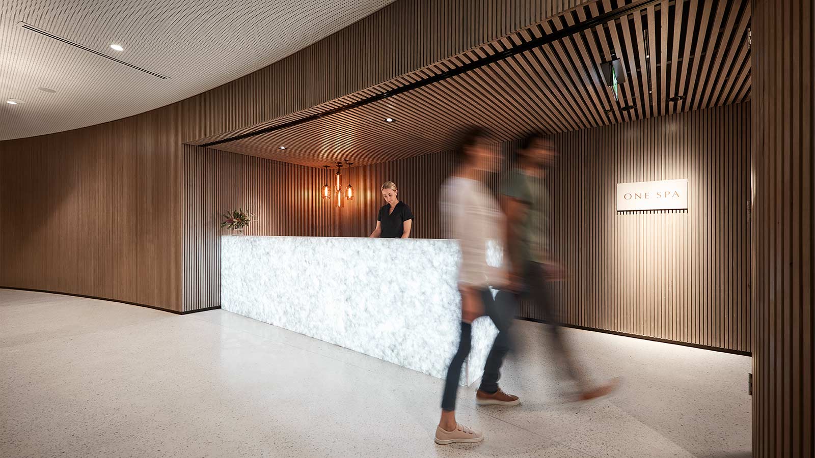 Two people walking into RACV Cape Schanck Resort's One Spa, with a receptionist at the desk behind them.