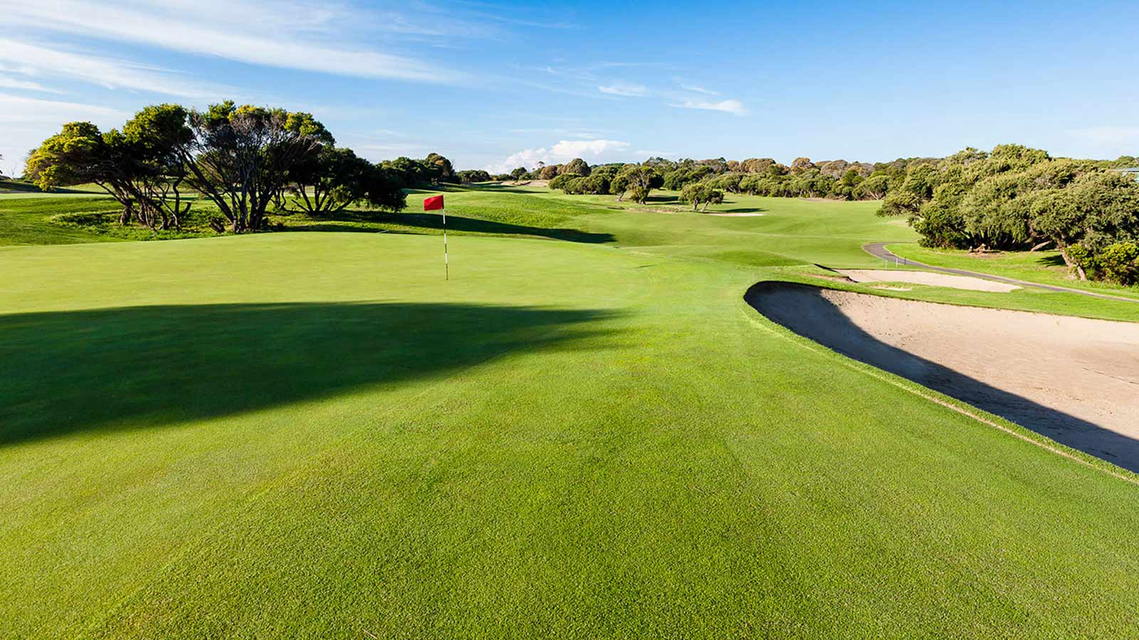 The sunlit vista of the golf course at RACV Cape Schanck Resort, with a green on the left and a sand trap on the right