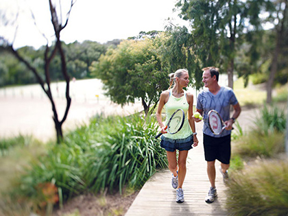 Couple jogging on a footpath and holding tennis racquets.